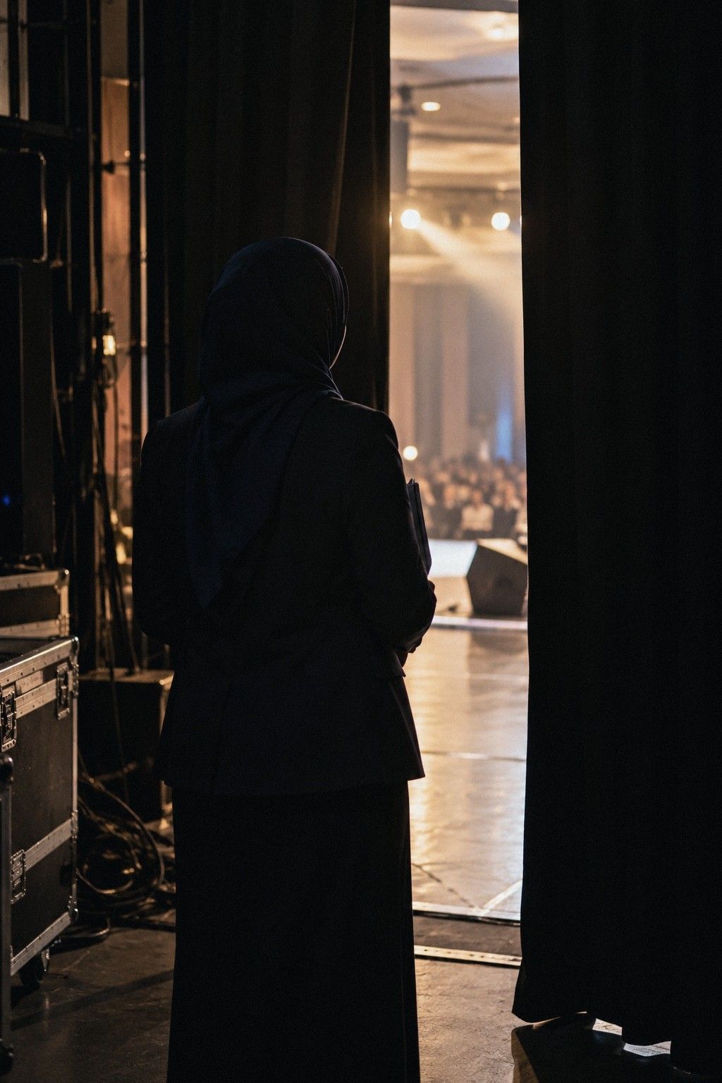 Siluet seorang wanita bertudung di belakang tirai pentas, menunggu namanya dipanggil